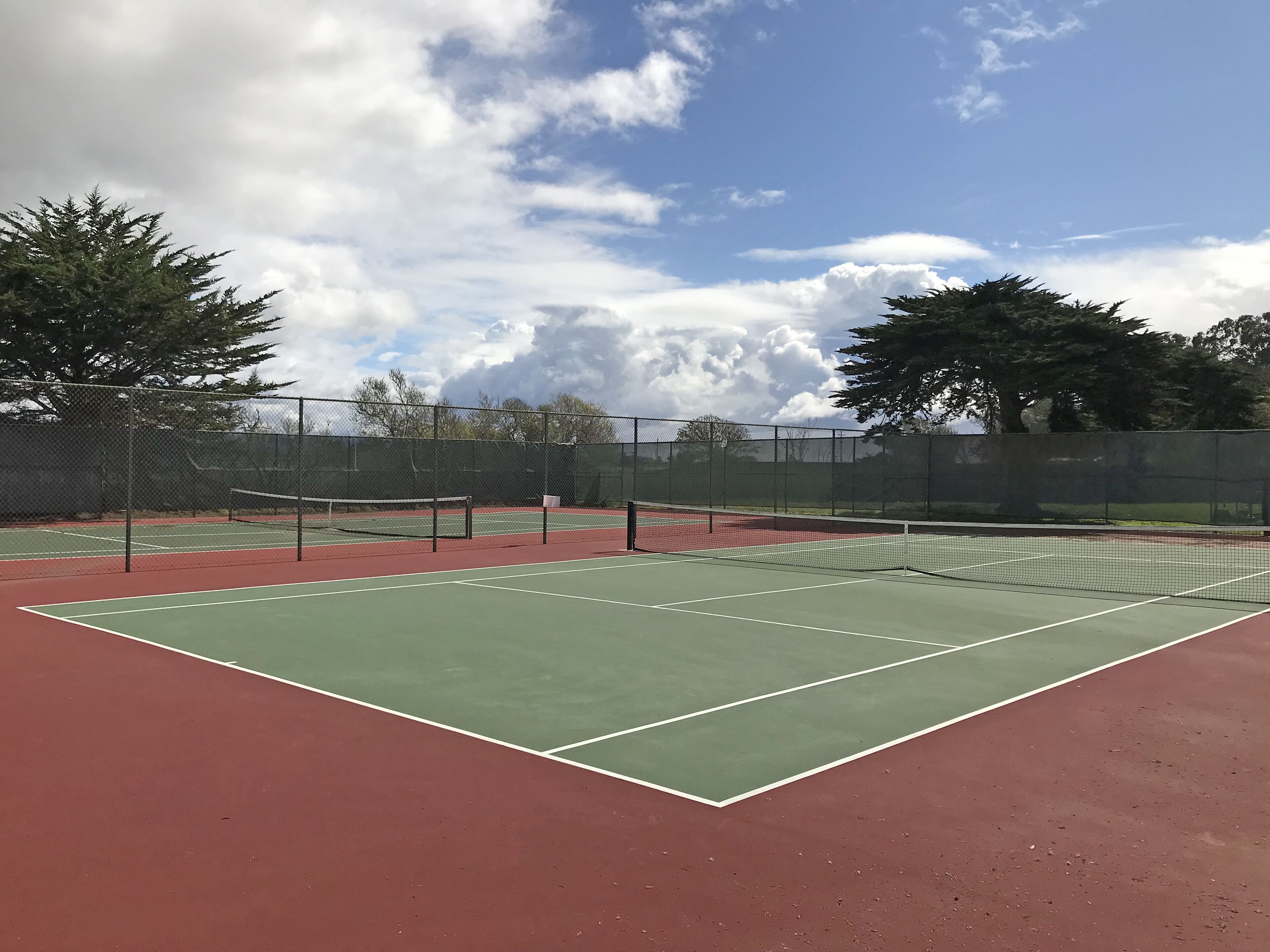 A tennis court with a net, surrounded by a fence and trees.