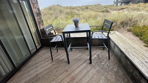 A wooden deck with a table and chairs, overlooking a grassy area and a building in the background. - Modern Beach Front Pajaro Dunes 1st Floor Condo - Yards From Beach/Gated Entry (Watsonville)