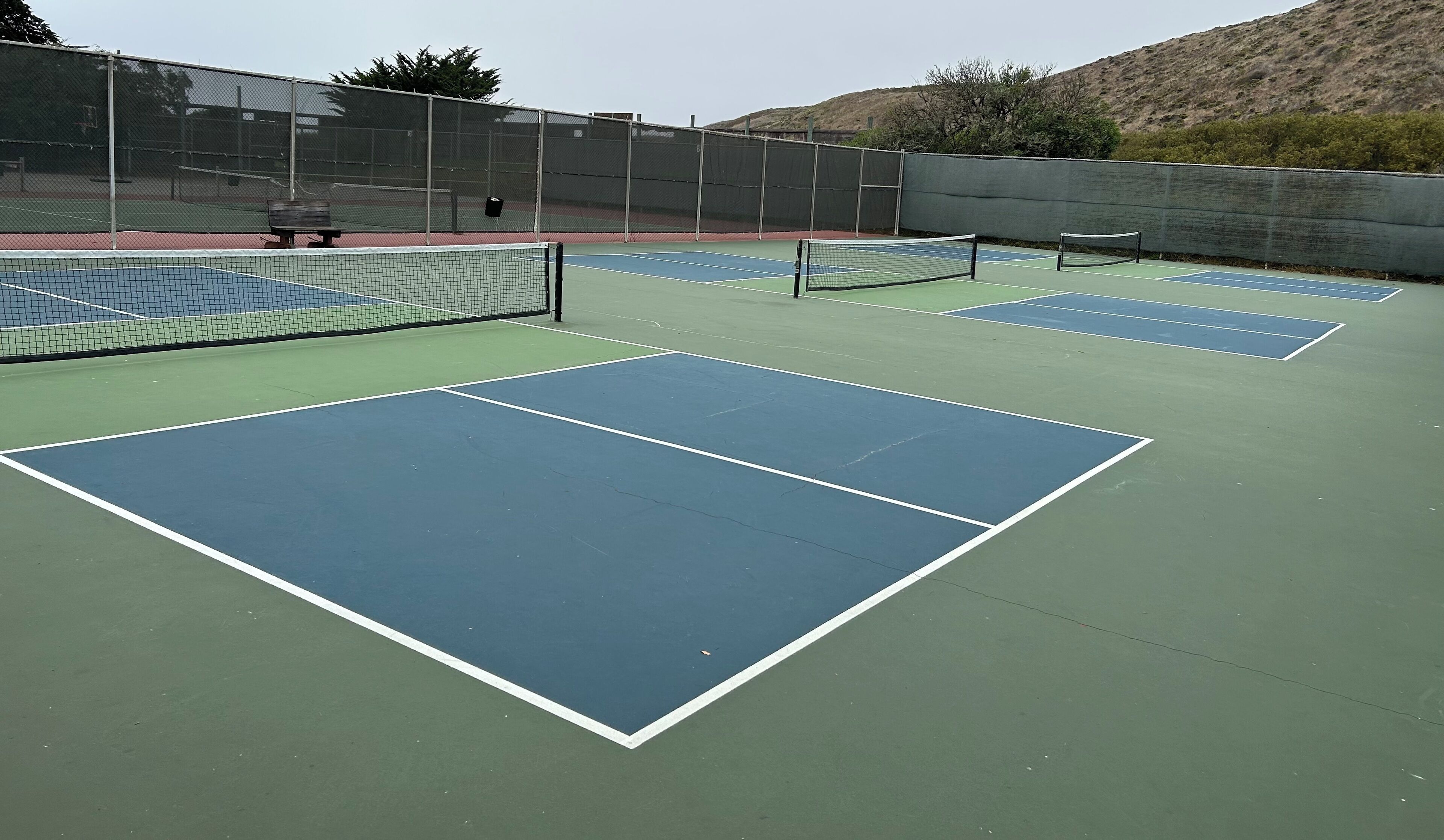 Un campo da tennis con più campi, panchine e una recinzione.