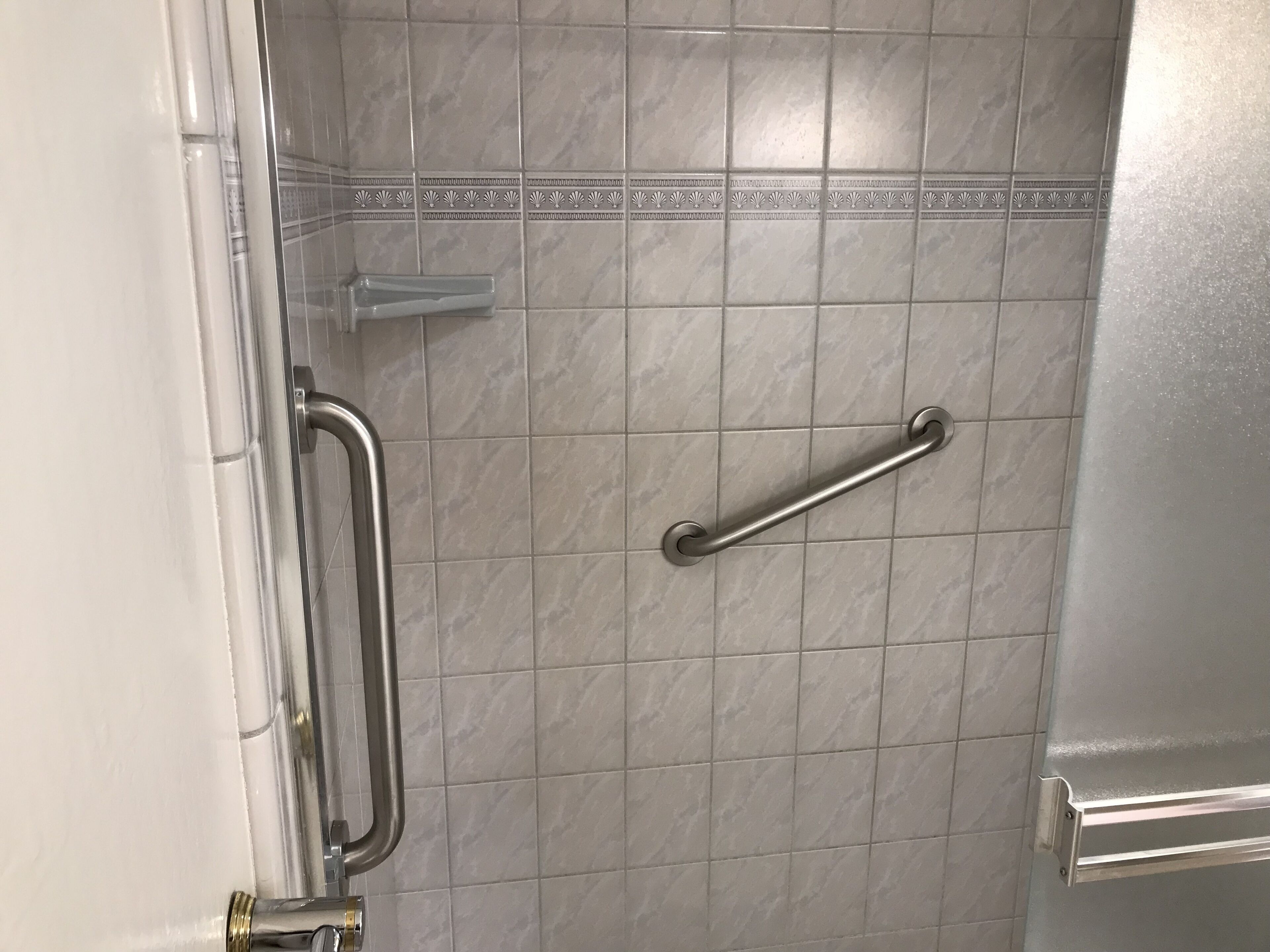 A bathroom with a handrail, a towel rack, and a tiled wall.