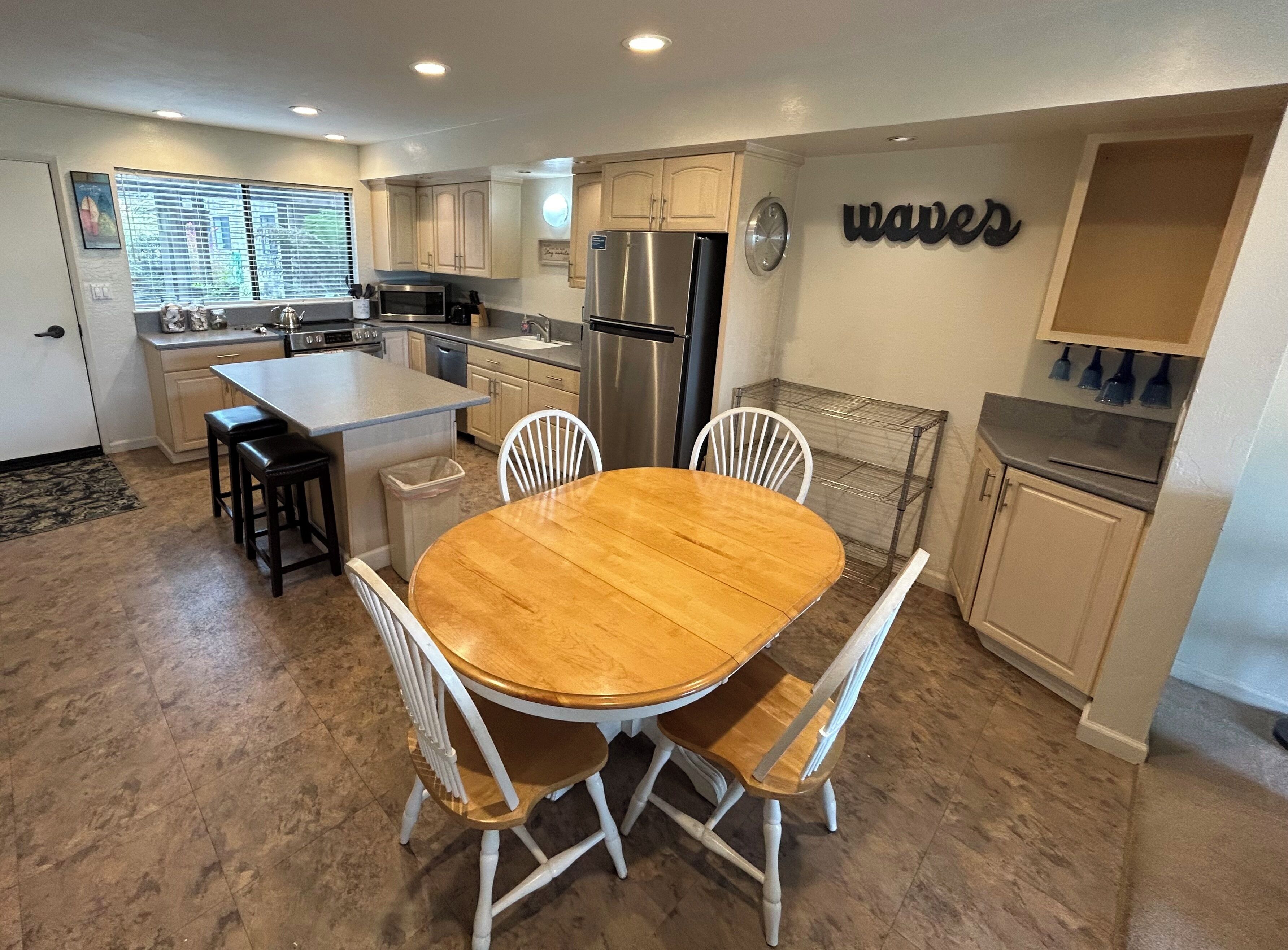 A modern kitchen with a central island, white cabinetry, and a dining area with a wooden table and white chairs.
