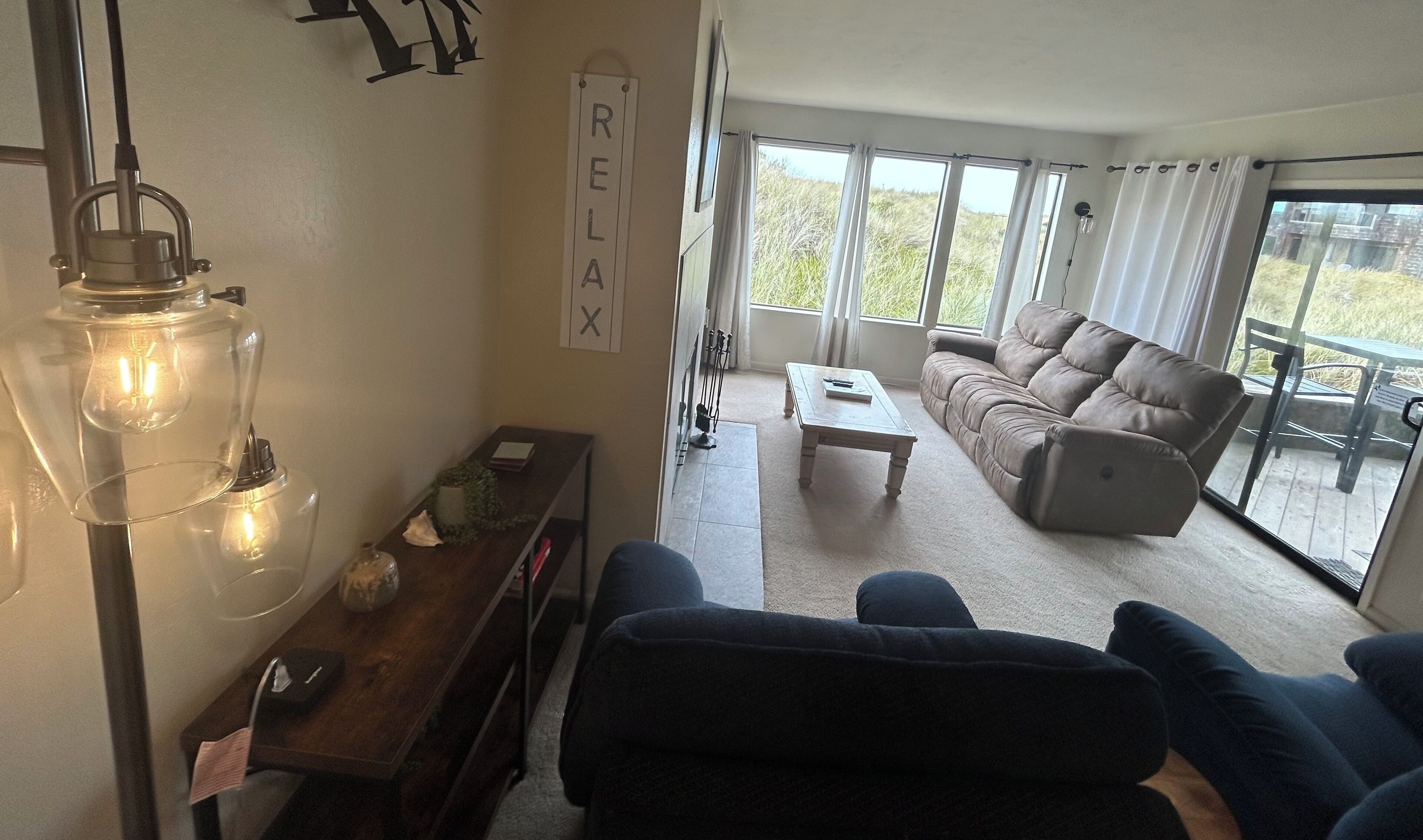 Un salon avec un canapé, une table basse et une lampe. Il y a une pancarte accrochée au mur sur laquelle on peut lire : « DÉTENTE ».