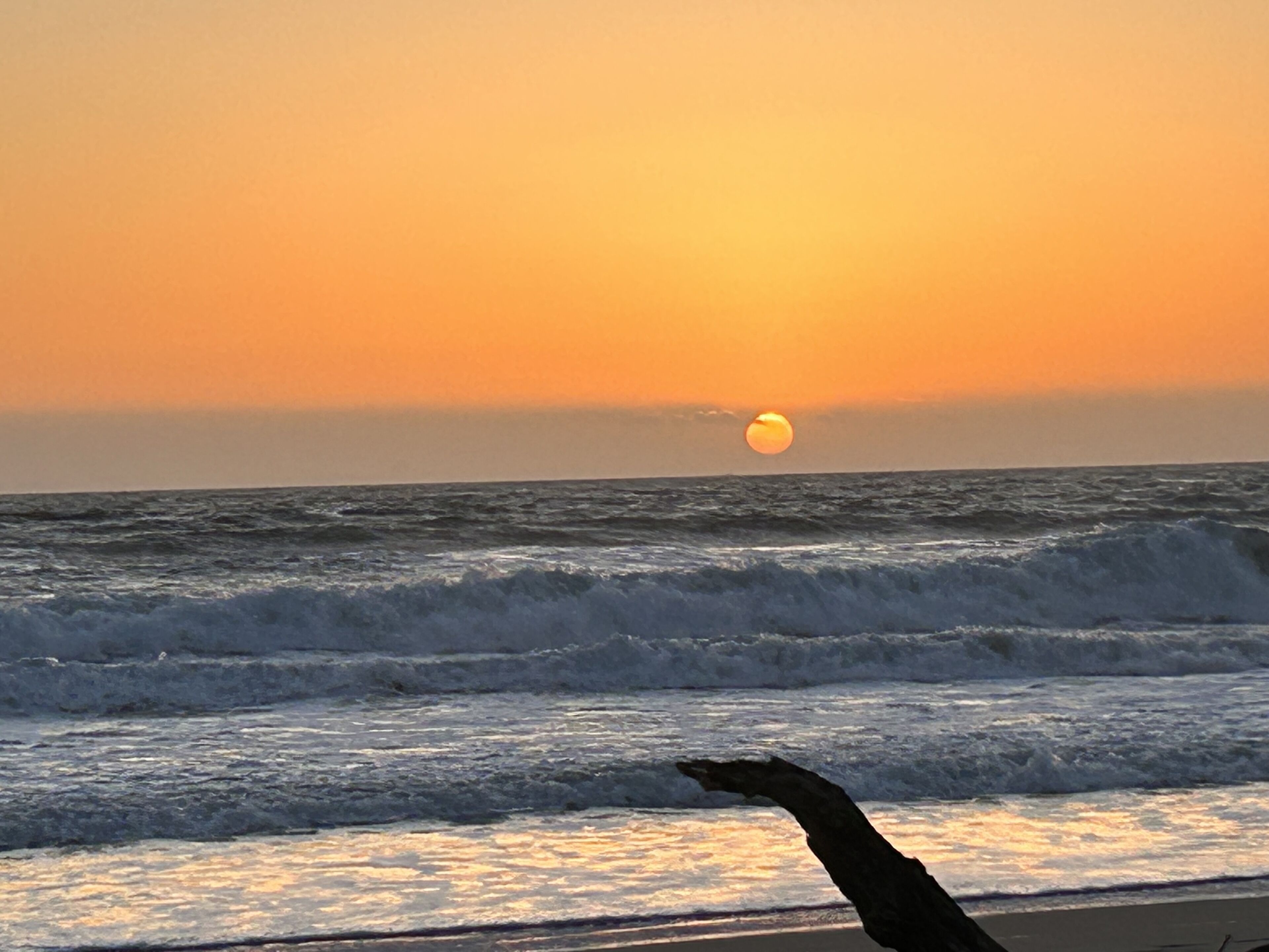 A sunset over the ocean with waves crashing onto the shore.