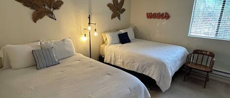 Ein Schlafzimmer mit zwei Betten, einem Nachttisch, einer Wandlampe und einem Fenster mit Jalousien.