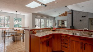A modern kitchen with a wooden island, large windows, and a dining area with a view. - Wooded Retreat - Steps to the Lake - Close to Town (Fennville)