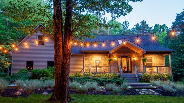 A two-story house with a porch, string lights, and a well-maintained garden. - Wooded Retreat - Steps to the Lake - Close to Town (Fennville)