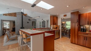 A modern kitchen with a central island, wooden cabinets, and a dining area with chairs. - Wooded Retreat - Steps to the Lake - Close to Town (Fennville)