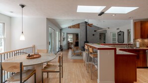 A modern kitchen with a central island, wooden flooring, and a dining area with a round table and chairs. - Wooded Retreat - Steps to the Lake - Close to Town (Fennville)