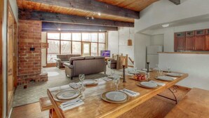 A dining area with a long wooden table set for a meal, a brick fireplace, and a modern kitchen in the background.