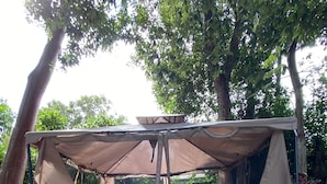 A covered outdoor seating area with a wooden deck and metal chairs, surrounded by trees and gravel. - Unique Houseboat on Dry Lot-Perfect Romantic Getaway Or Family Friendly & Pet OK (Key Largo)