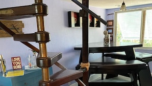 A spiral staircase with a wooden finish, a blue dresser with drawers, a sign reading "LOVE YOU MORE", and a dining area with a table and chairs in the background. - Unique Houseboat on Dry Lot-Perfect Romantic Getaway Or Family Friendly & Pet OK (Key Largo)