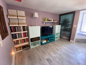 A living room with a TV, bookshelves, and a door with a palm tree mural.