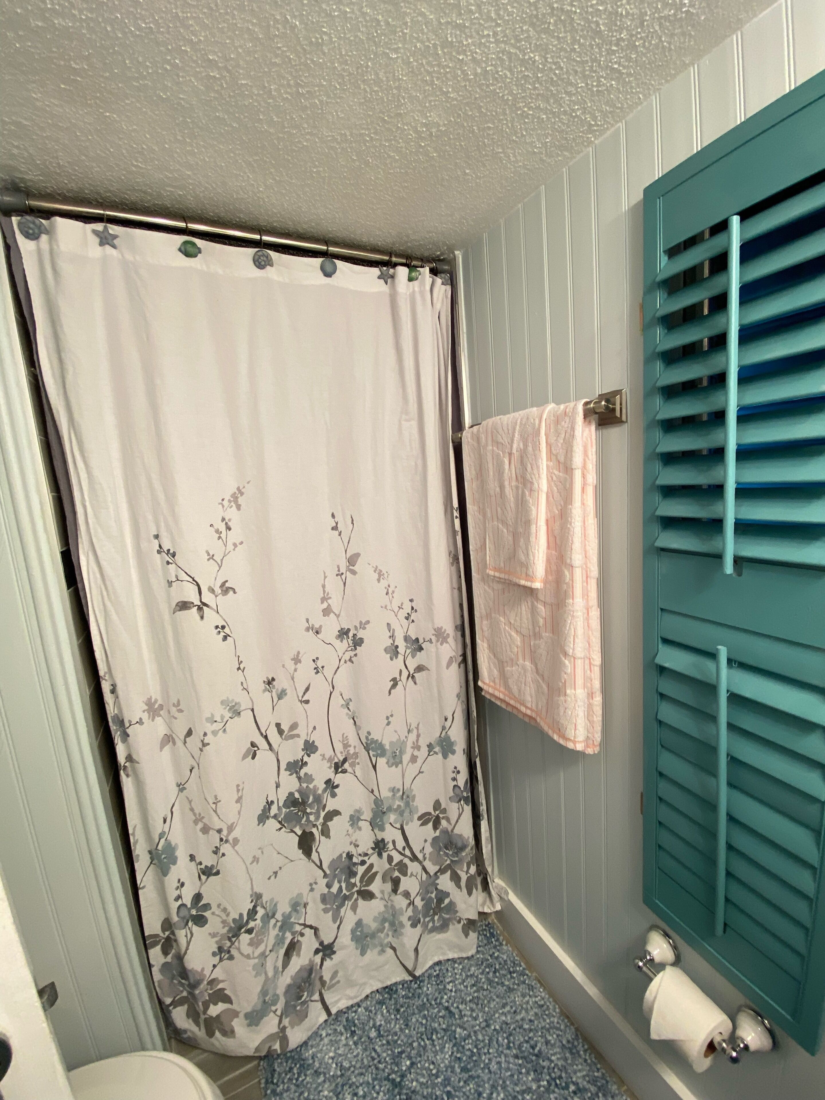 Une salle de bain avec un rideau de douche orné d’un motif floral, une serviette suspendue à un porte-serviettes et des toilettes dotées d’un distributeur d’essuie-tout.