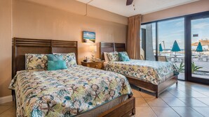 A hotel room with two beds, a ceiling fan, a beach view, and a large window.