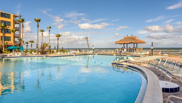 A pool area with lounge chairs and a thatched umbrella, overlooking the ocean.
