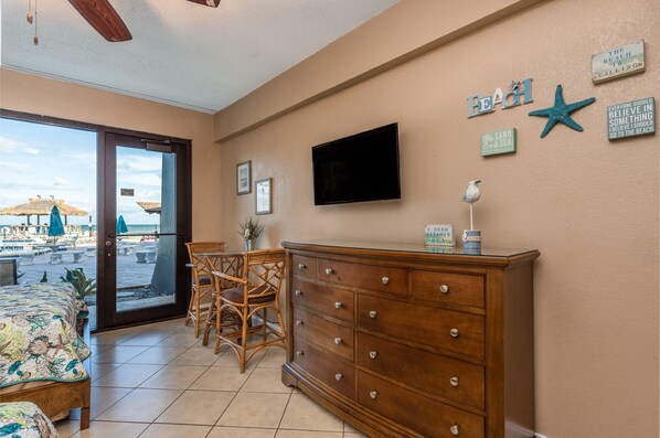 A room with a beach view, a wooden dresser, wicker chairs, a flat-screen TV, and various wall decorations including a starfish and a sign that says "The Beach is Calling". - First Floor Amazing Updated Ocean Front Studio!! "SUMMER MEGA SALE" POOL OPEN (Daytona Beach Shores)