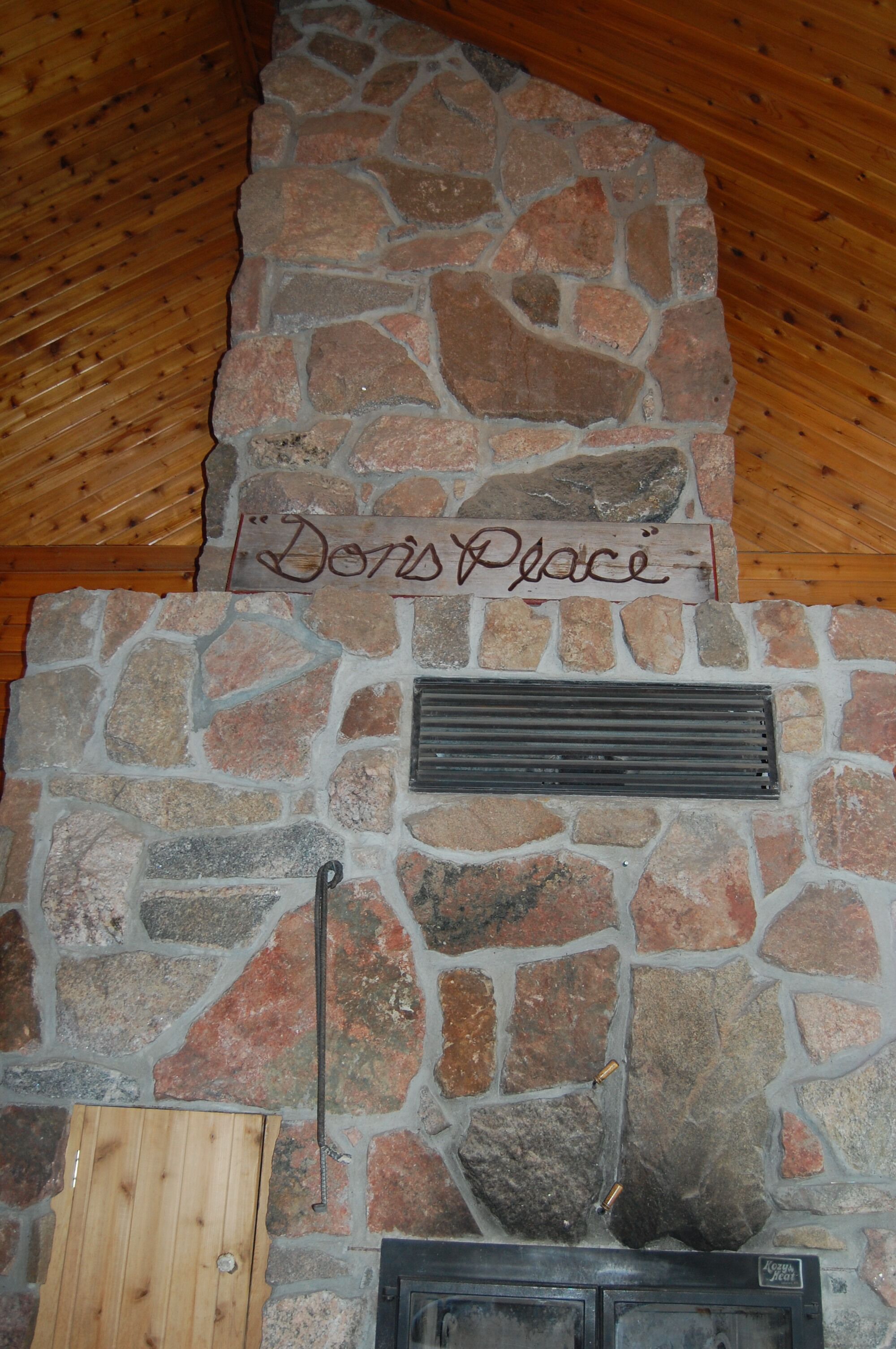A stone fireplace with a metal vent and a wooden sign above it.
