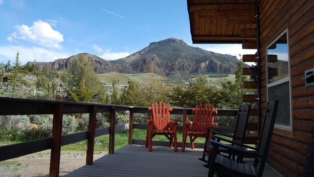 Una terraza de madera con sillas Adirondack que da a un paisaje montañoso.