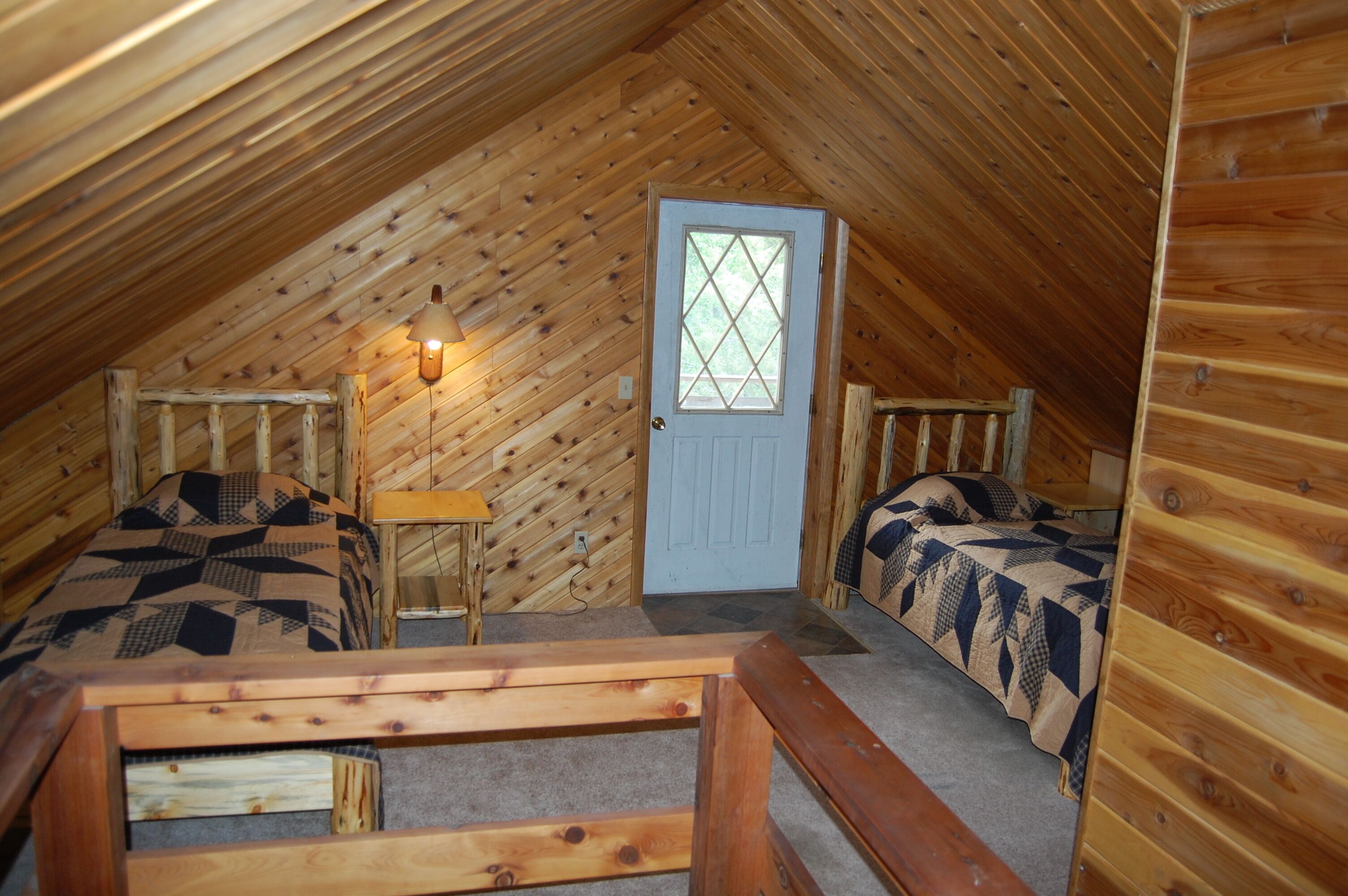 A cozy attic bedroom with two beds, a small table, and a door with a window.