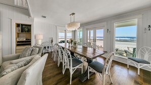 A spacious dining area with a wooden table and white wicker chairs, overlooking a beach.