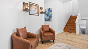 Ein modernes Wohnzimmer mit zwei Ledersesseln, einer Holztreppe und Kunstwerken an den Wänden.
