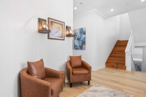Un salon moderne avec deux fauteuils en cuir, un escalier en bois et des œuvres d’art accrochées aux murs.