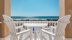 Ein Balkon mit weißen Stühlen und einem Tisch mit Blick auf einen Strand.