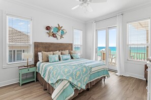A bedroom with a large bed, a nightstand, a ceiling fan, and a view of the ocean through the windows.
