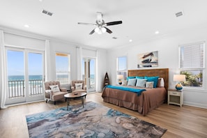 Une chambre spacieuse avec un grand lit, un ventilateur de plafond et une vue sur l’océan depuis les portes du balcon.