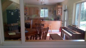 A kitchen with wooden cabinets, a dining table with chairs, a piano, and a window with a view of trees.