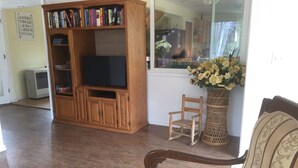 A living room with a wooden entertainment center, a television, a wicker chair, and a large vase with flowers.