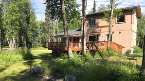 A cabin with a deck, surrounded by trees and a gravel path.