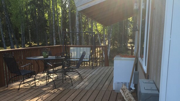 A wooden deck with outdoor furniture, a welcome sign, and a view of trees.