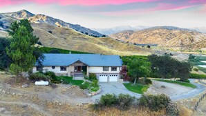 A house with a blue roof, stone foundation, and a garage. It is surrounded by a green lawn and a dirt path. - Ranch Getaway in the foothills of the Sierras (Springville)