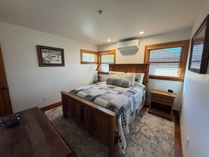 Ein Schlafzimmer mit einem hölzernen Bett, einem Nachttisch, einer Lampe und einem Fenster mit Jalousien.