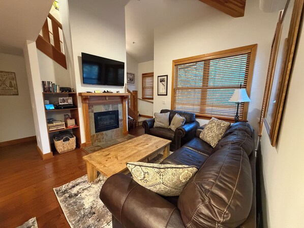 A living room with a fireplace, a leather sofa, a wooden coffee table, and a television mounted on the wall. - Remodel Oct 2026 - Deer Valley Townhouse, with Hot Tub & Steps Away from the Bus (Park City)