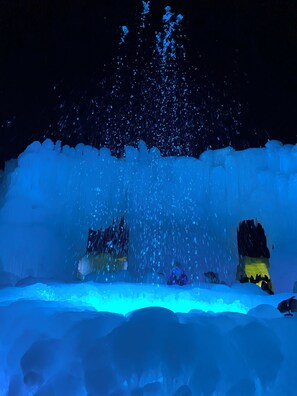 Een nachtscène met een grote, verlichte ijs sculptuur op de voorgrond, met een waterval effect.