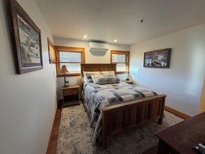 Un dormitorio con una cama de madera, dos mesitas de noche, una lámpara y un cuadro en la pared.