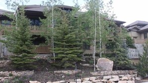 A multi-story building with a stone foundation, wooden deck, and a large rock centerpiece. - Deer Valley Townhouse, with New Private Hot Tub Just Steps Away from the Bus (Park City)