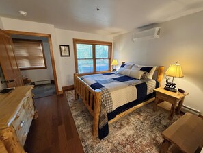 A bedroom with a wooden bed, a nightstand with a lamp, a window with blinds, and a door. - Remodel Oct 2026 - Deer Valley Townhouse, with Hot Tub & Steps Away from the Bus (Park City)