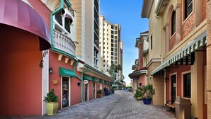 A narrow street lined with buildings, some with balconies and awnings, and a few potted plants.