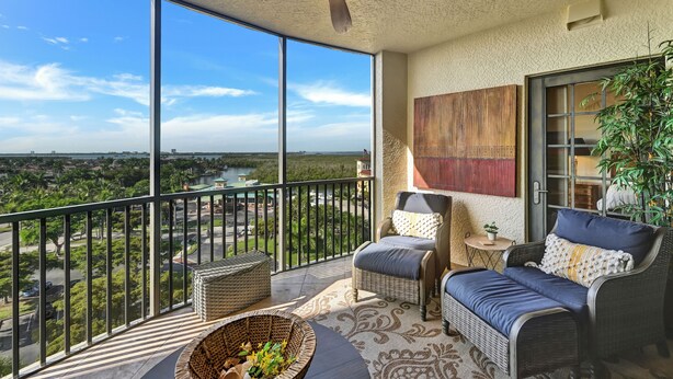 A balcony with wicker furniture, a view of a river and greenery, and a ceiling fan.
