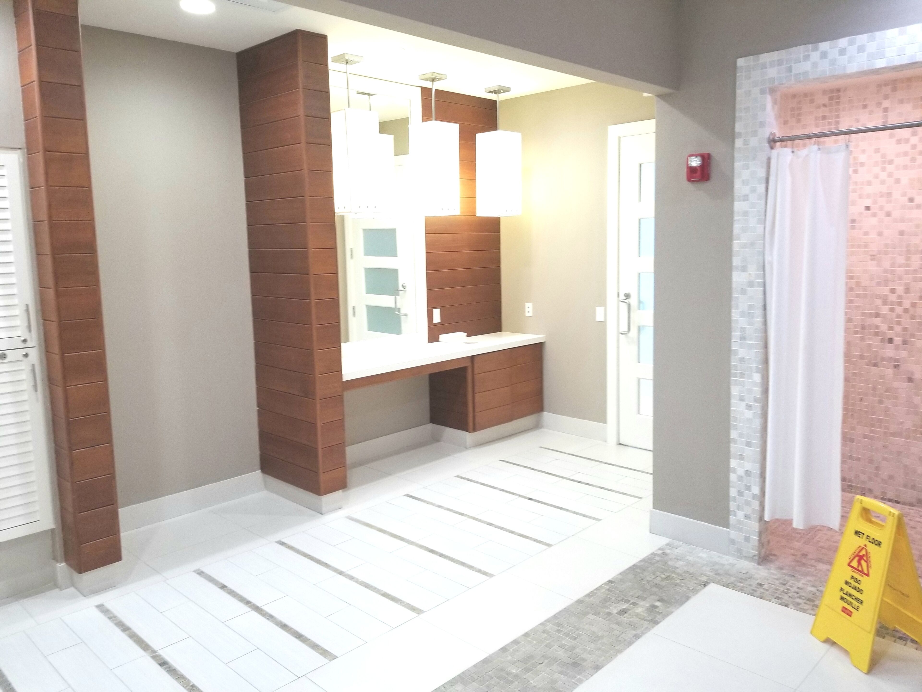 Un baño moderno con una pared de acento de madera, un lavabo blanco y una zona de ducha con suelo de baldosas.