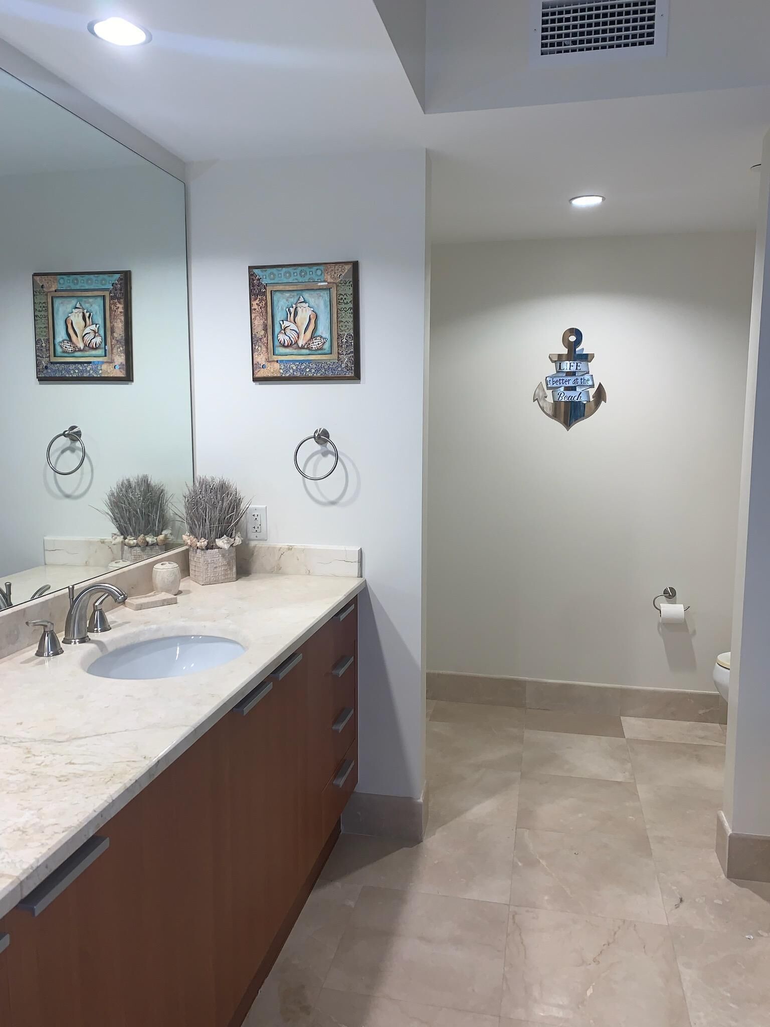 Un baño moderno con un espejo grande, dos obras de arte enmarcadas, un ancla decorativa y un lavabo de mármol.
