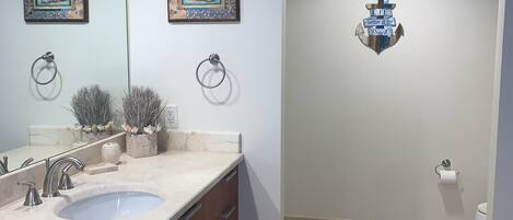 Un baño moderno con un espejo grande, dos obras de arte enmarcadas, un ancla decorativa y un lavabo de mármol.