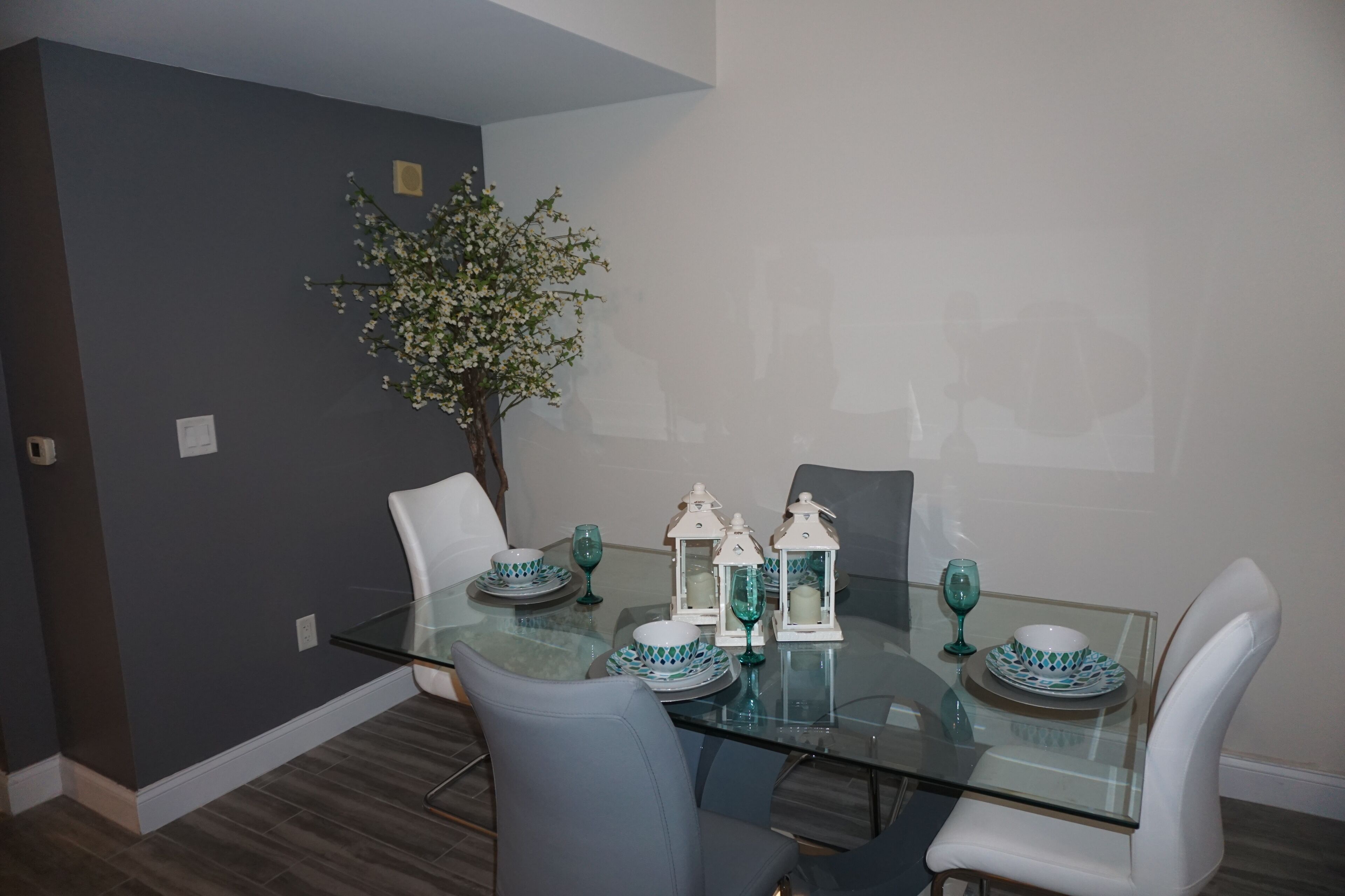 A dining area with a glass table, white chairs, teal and white tableware, and a small potted plant.
