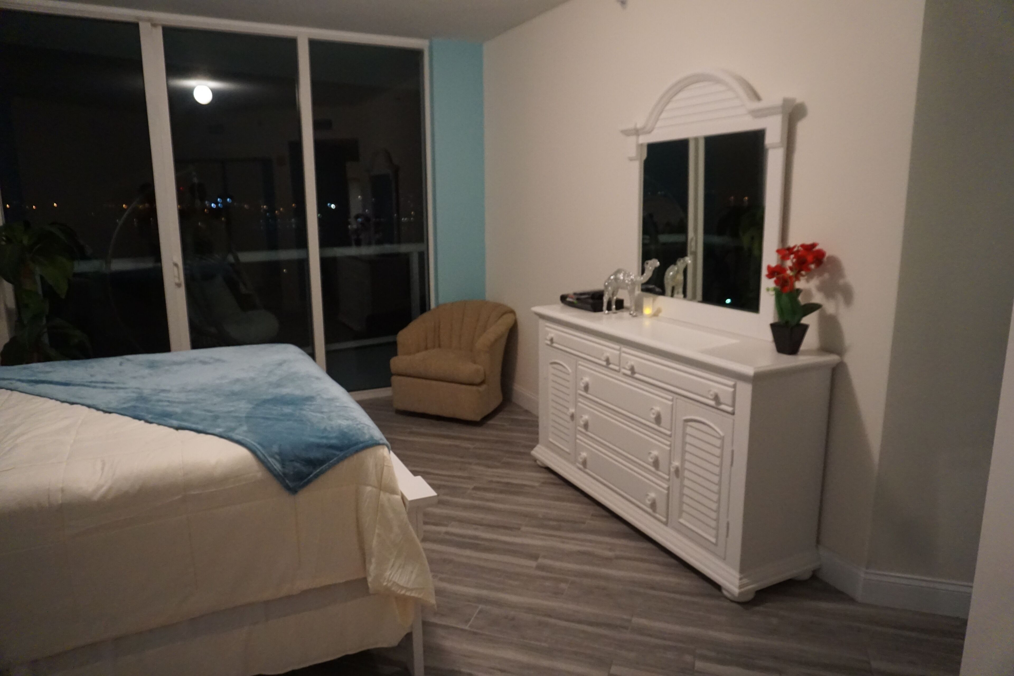 Ein Schlafzimmer mit Bett, Kommode, Stuhl und einem großen Fenster.