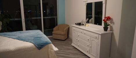 Ein Schlafzimmer mit Bett, Kommode, Stuhl und einem großen Fenster.