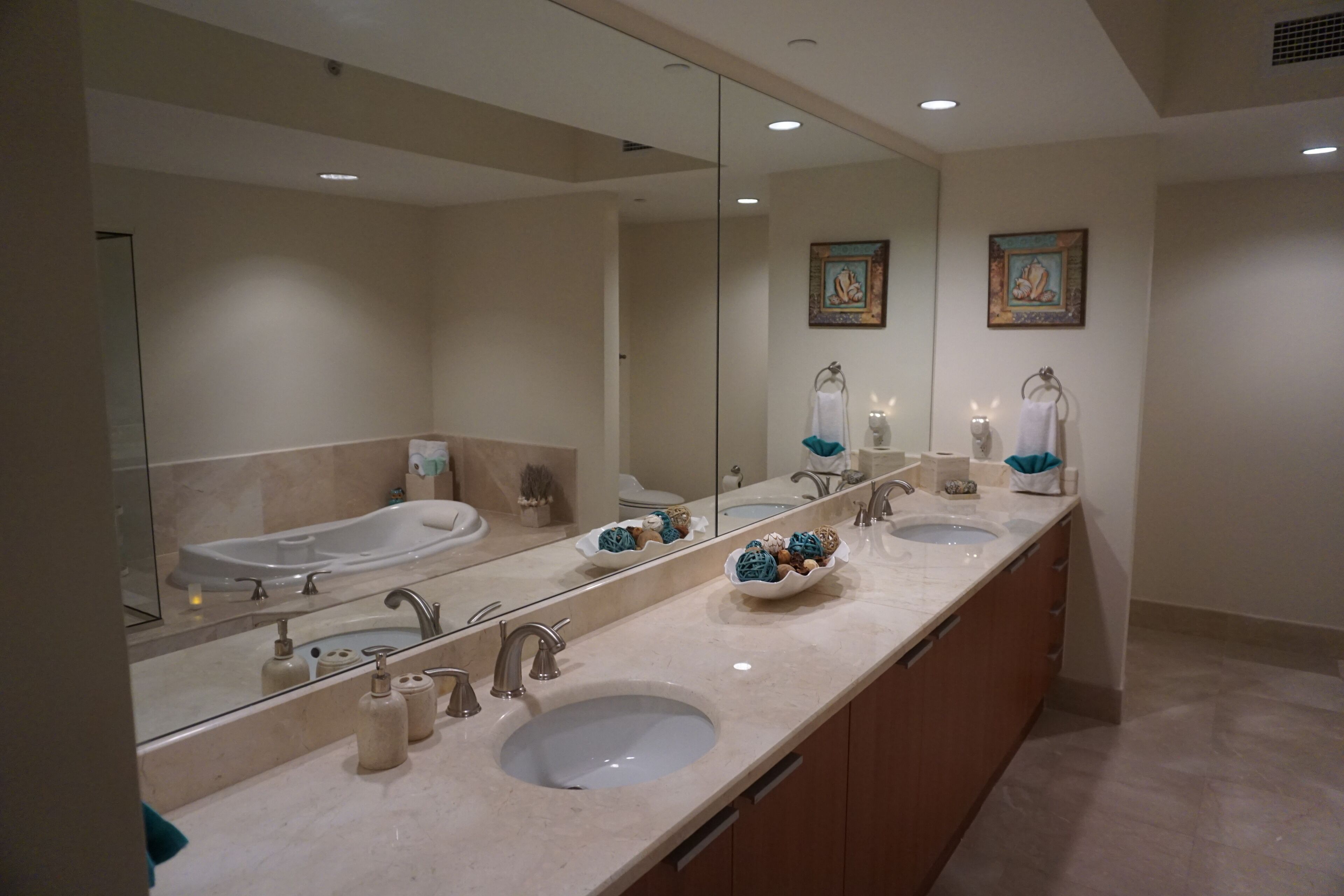 Une salle de bain moderne avec un meuble-lavabo à deux vasques, un grand miroir et deux œuvres d’art encadrées accrochées au mur.