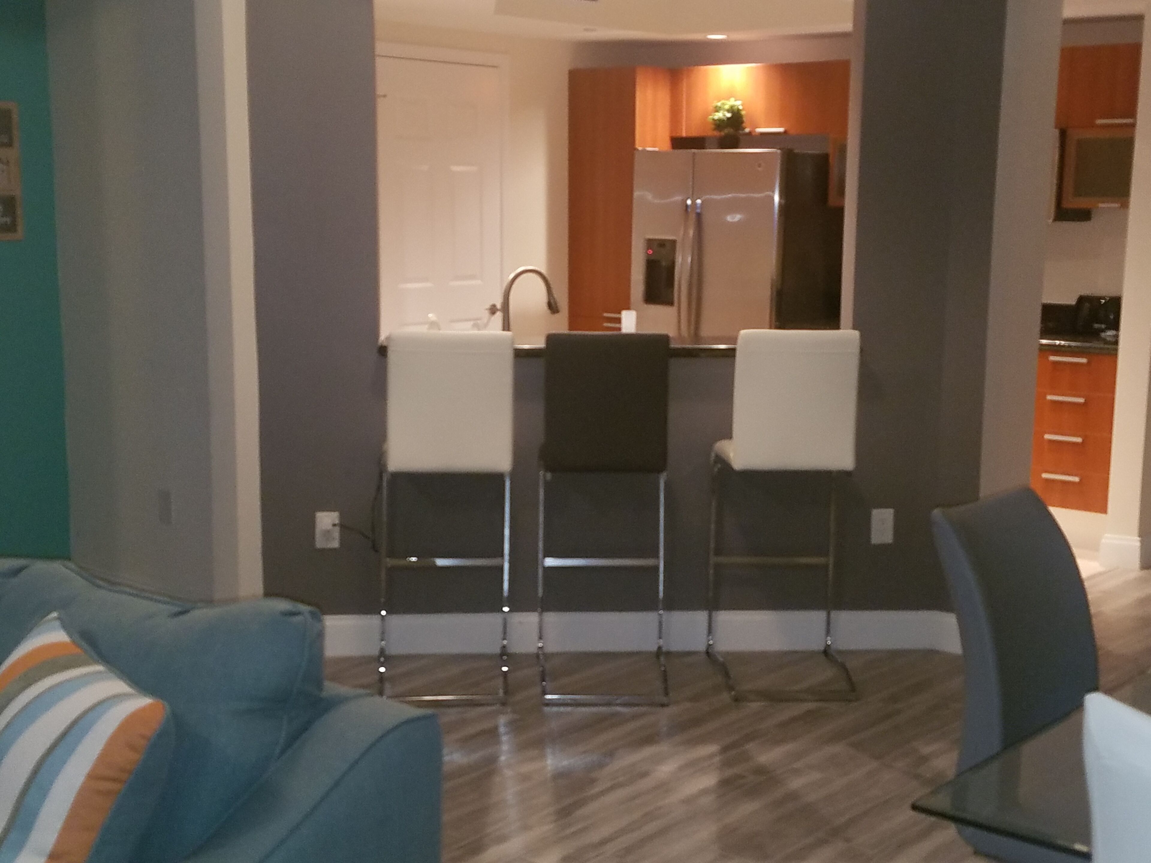 A modern kitchen with a refrigerator, sink, and bar stools.